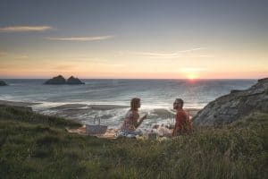 Sunset at Holywell Bay looking out to Gull Rocks with couple having picnic on the cliffs