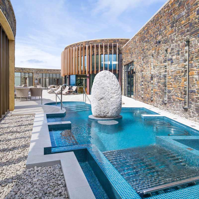 Outdoor spa pool with modern stone walls, a large white sculpture, and sun loungers under a bright sky. Spa Days at Headland Hotel, Newquay