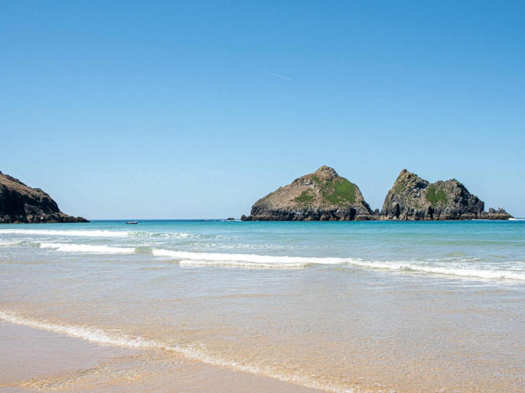 Scenic view of Gull Rocks at Holywell Bay in Cornwall, with clear blue skies, gentle waves, and golden sand — just a short walk from Trevornick Holiday Park.